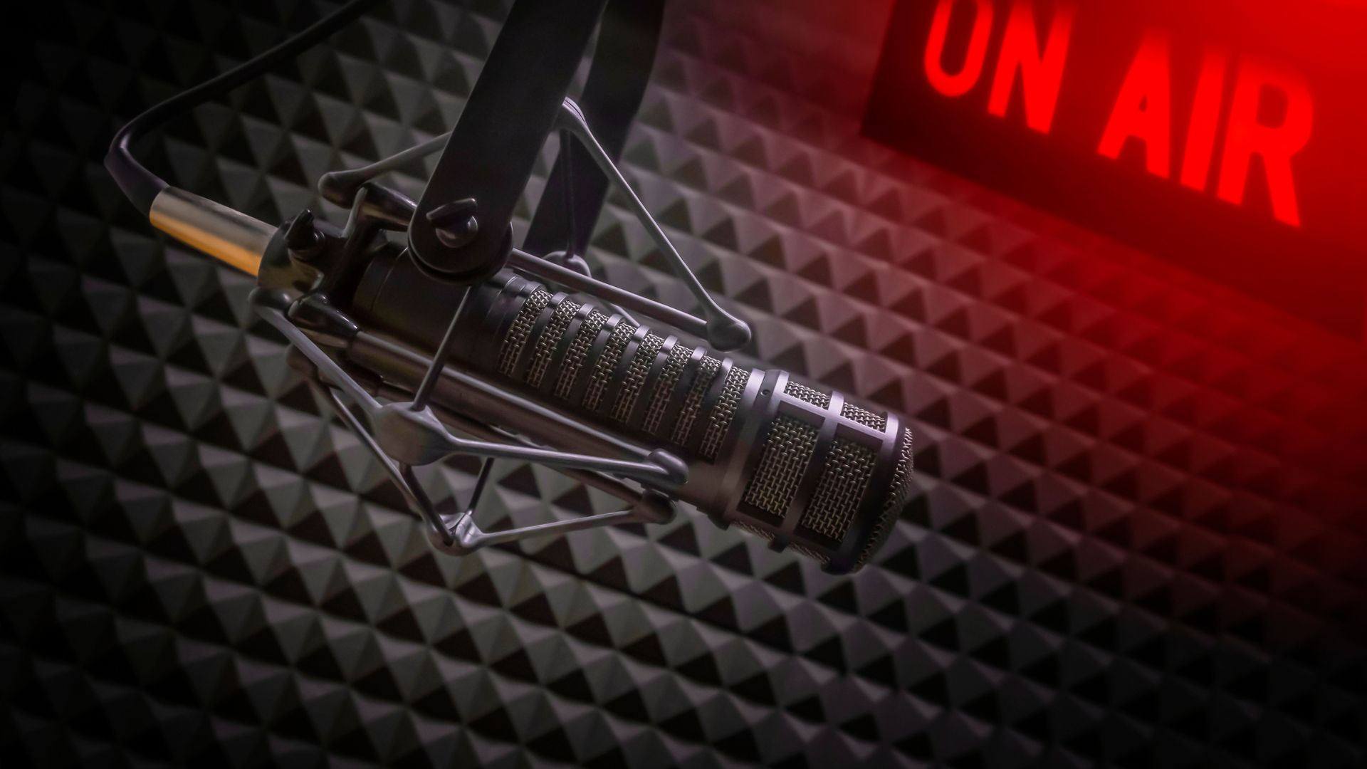 This image shows a professional microphone in a radio station studio with an on air sign.