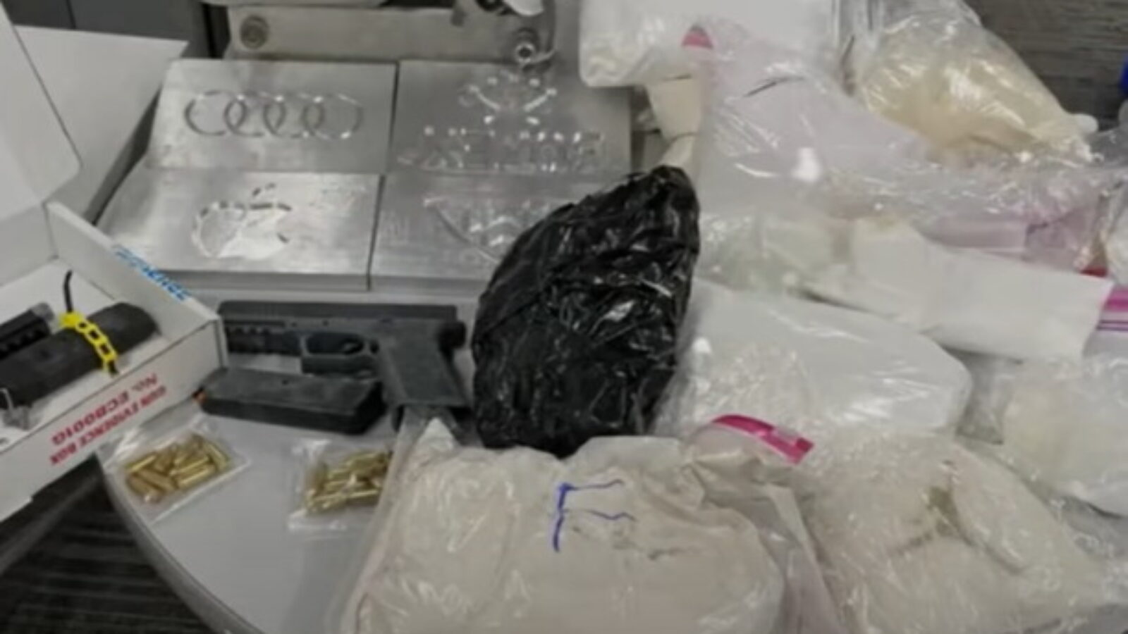 Display of confiscated illegal drugs and firearms, including packaged substances and ammunition on a table.