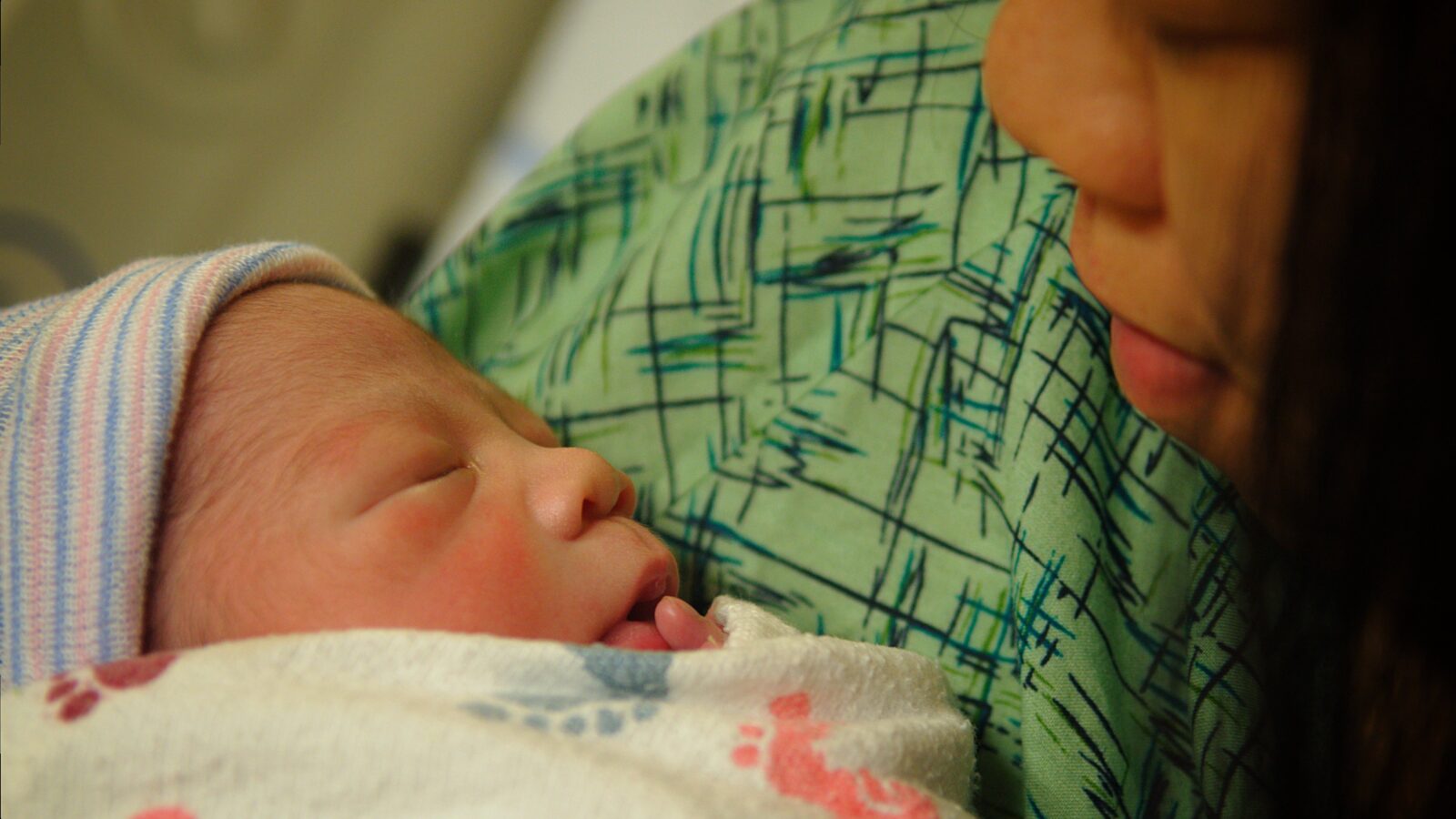Newborn baby peacefully sleeping in a hospital blanket while being cradled by a caregiver, showcasing a tender moment of connection.
