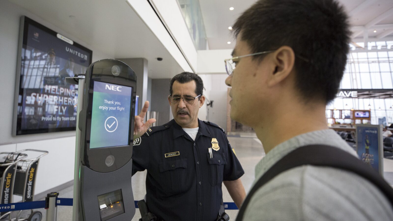 Airport security officer assisting a traveler at a self-service kiosk displaying a flight confirmation message.