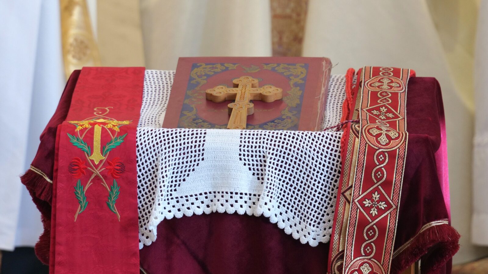 Wooden cross on a decorative altar cloth with embroidered red and white elements, symbolizing a religious setting.