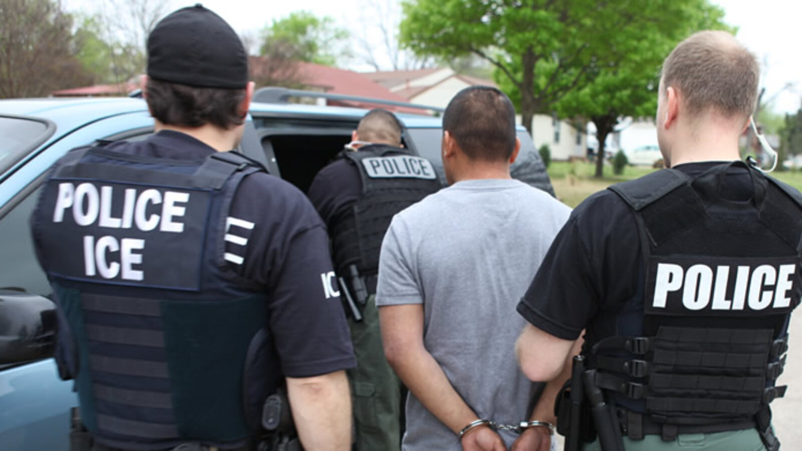 Law enforcement officers in tactical gear apprehending an individual during an immigration enforcement operation.