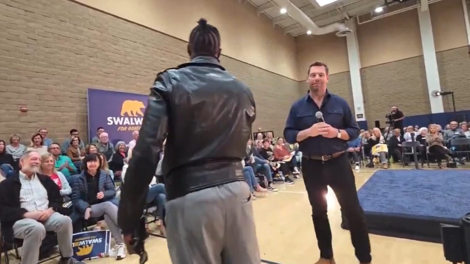 Audience engagement event featuring a speaker and attendees, with a backdrop promoting Swalwell for Governor campaign.