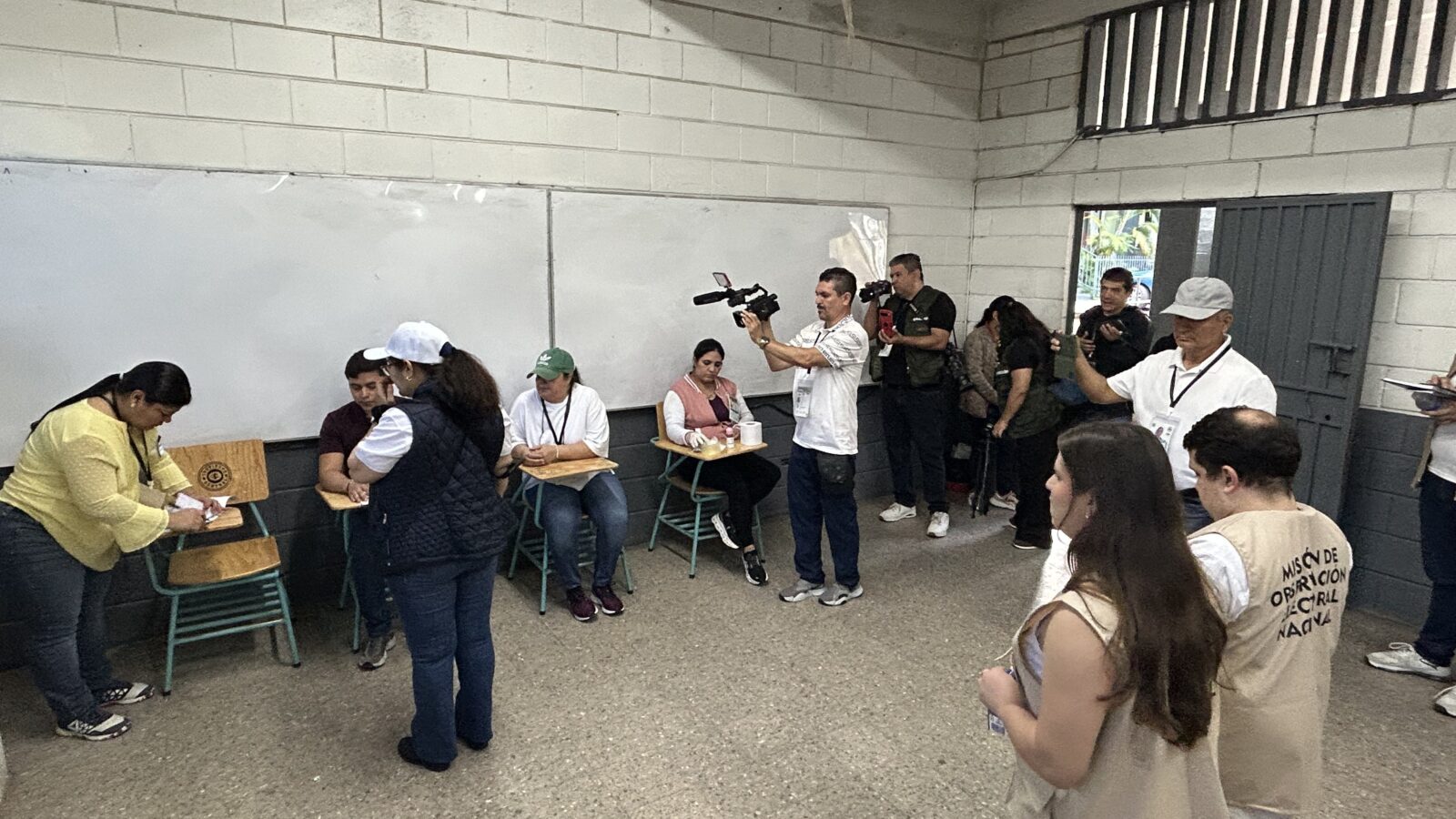 Election officials and volunteers interact in a classroom setting, documenting the voting process during an election event.
