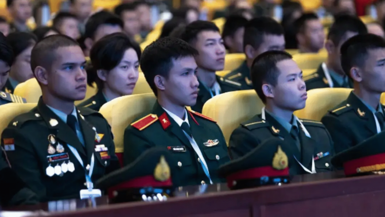 Military personnel attentively listening during a conference, showcasing a diverse group of soldiers in uniform seated in a large auditorium.