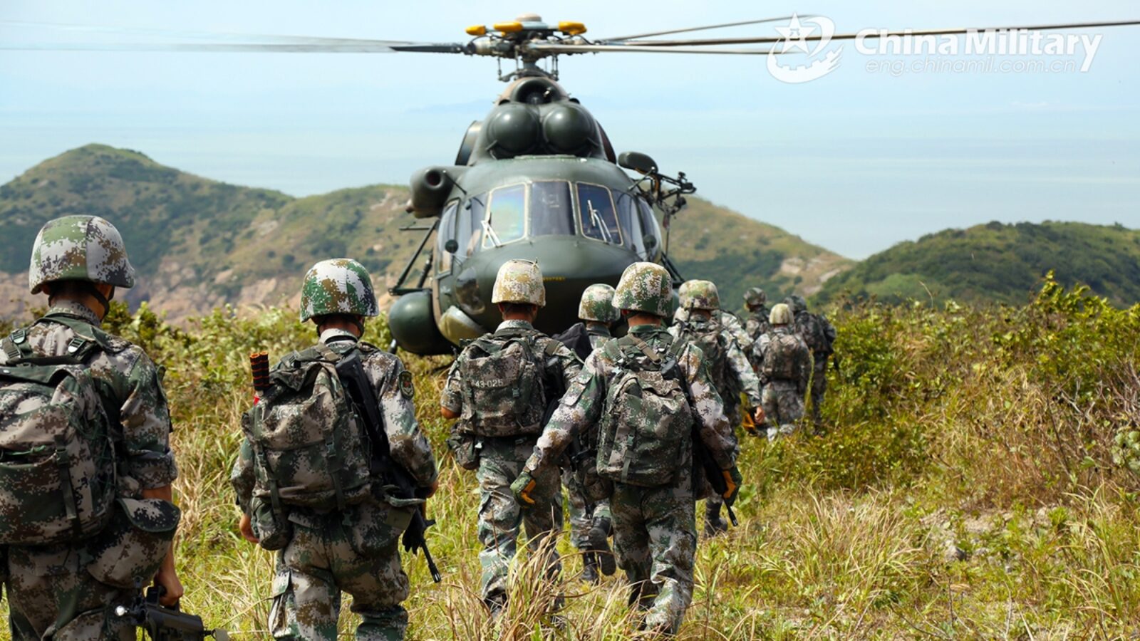 Chinese soldiers approach a military helicopter on a hillside, showcasing a training exercise in a mountainous landscape.