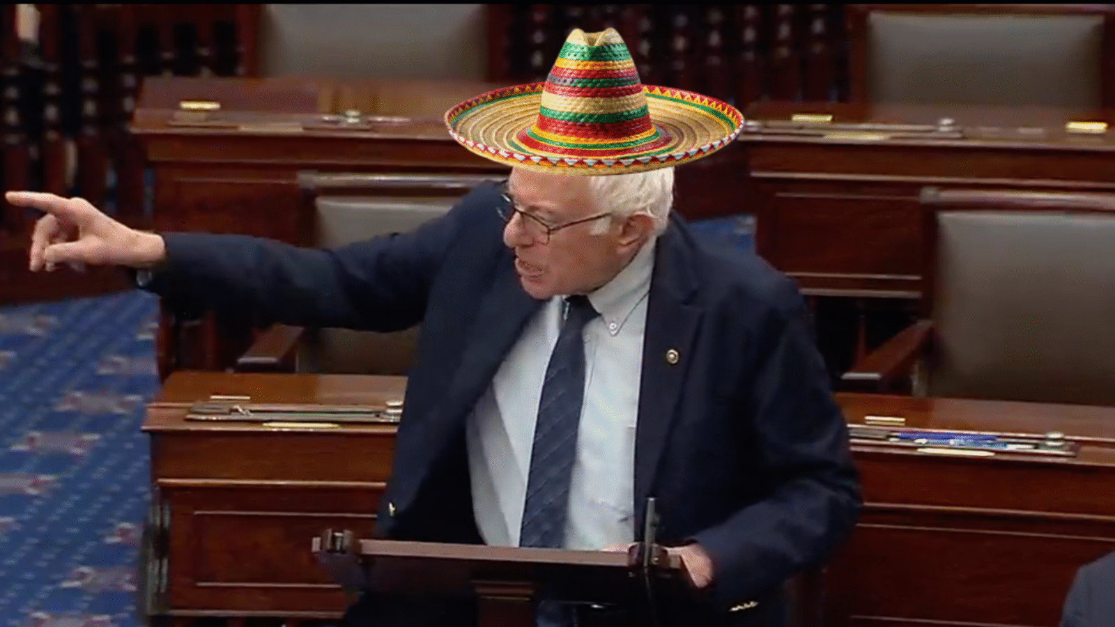 Senator passionately speaks at a podium in Congress while wearing a colorful sombrero, emphasizing a point during a debate.