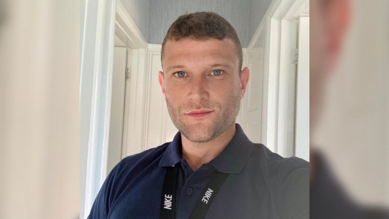 Man in a navy polo shirt with a Nike lanyard poses for a selfie in a well-lit hallway.