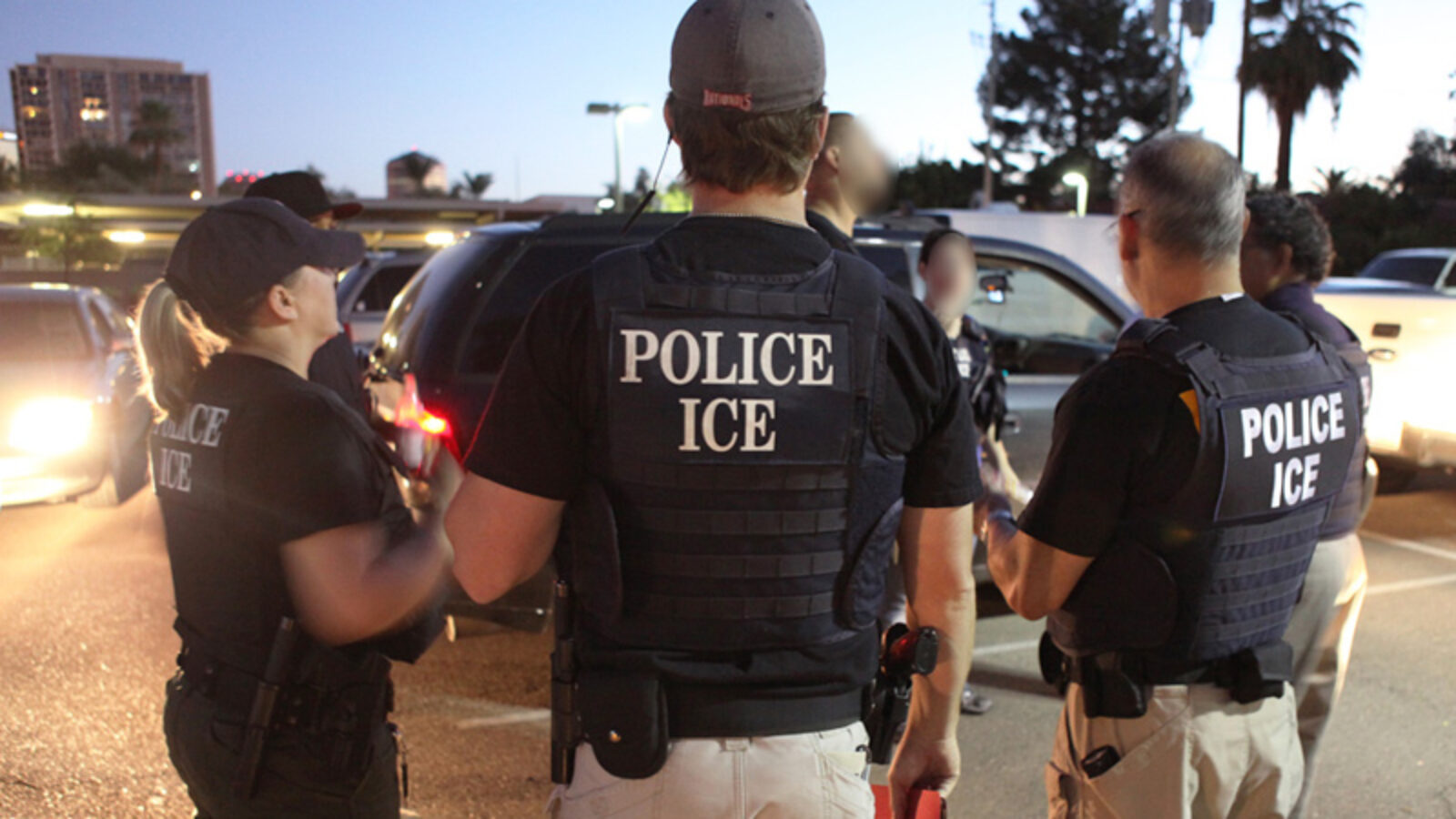 Police officers from ICE engage in a discussion during a night operation in a parking lot, emphasizing law enforcement activities.