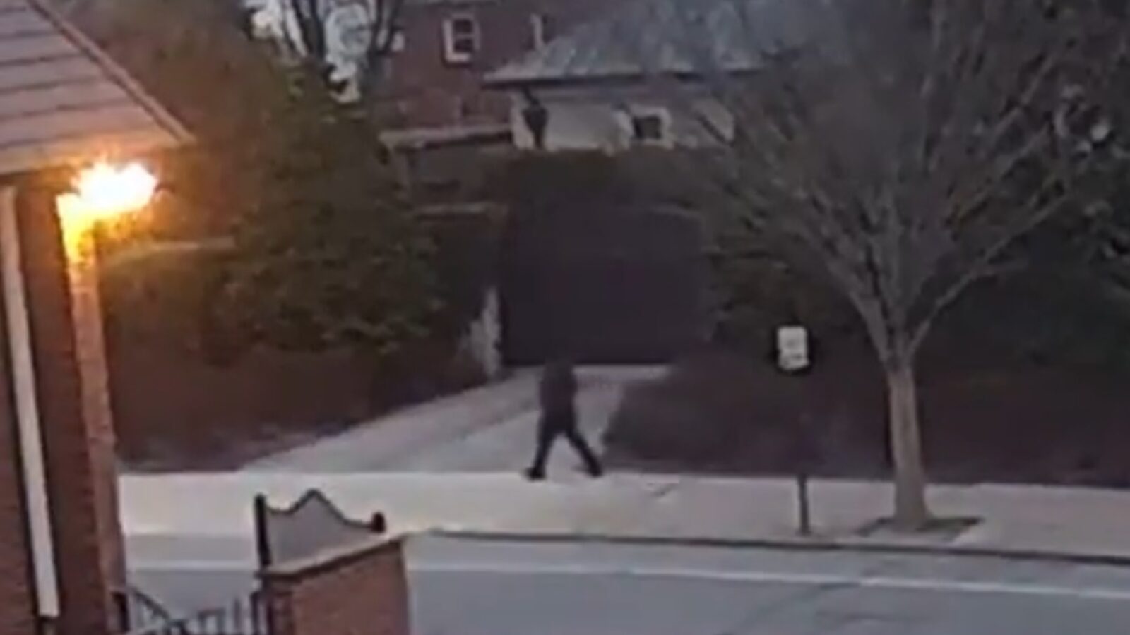 A person walking along a sidewalk near residential homes during early morning hours, with a streetlight illuminating the area.