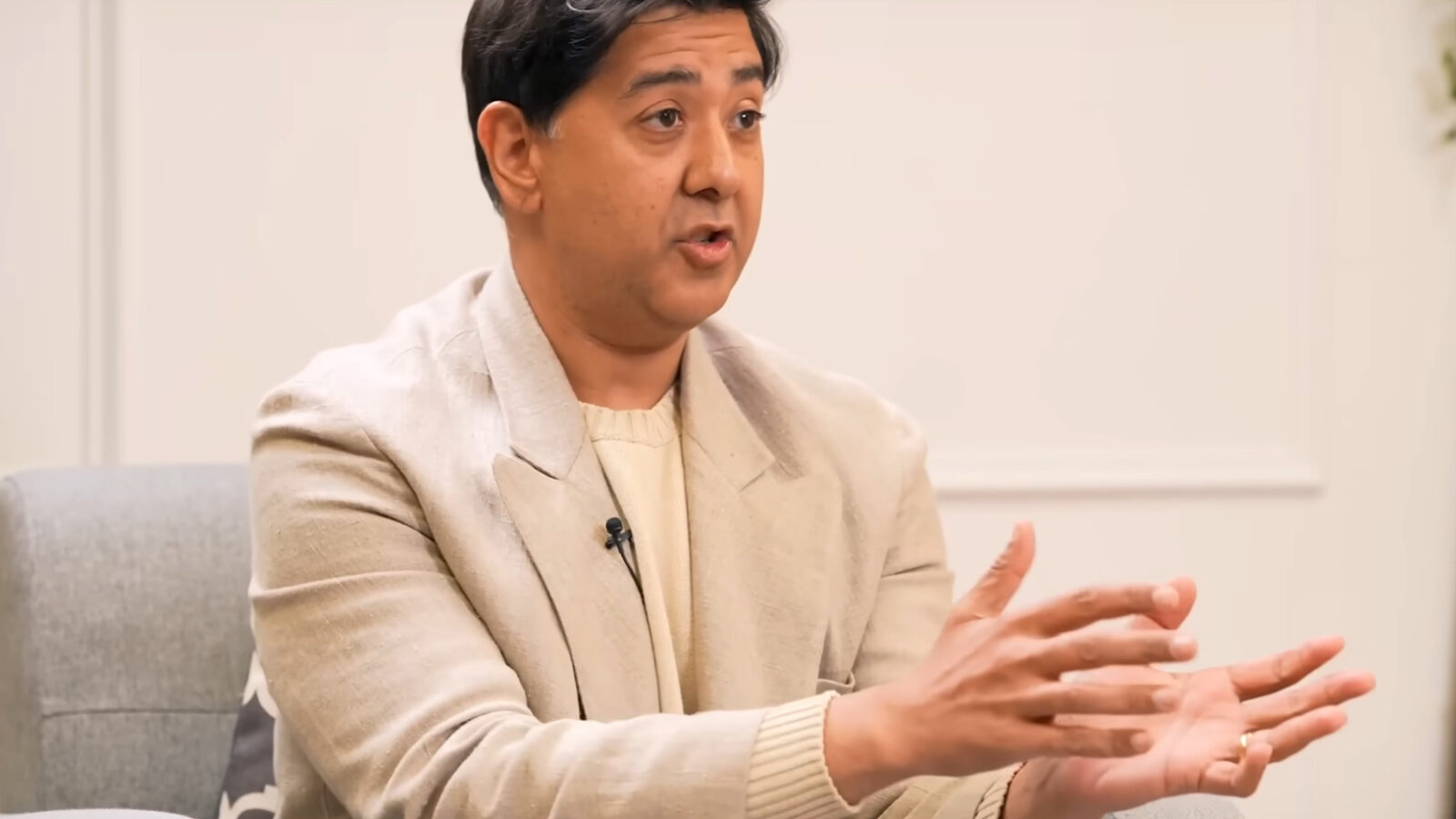 Person in a beige blazer gestures while speaking during an interview, emphasizing key points in a modern office setting.