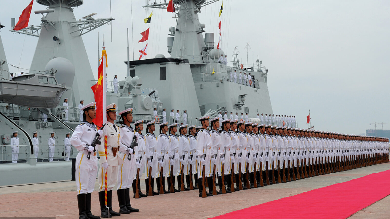 Chinese naval ceremony featuring uniformed sailors lined up in formation, showcasing military precision and naval vessels in the background.