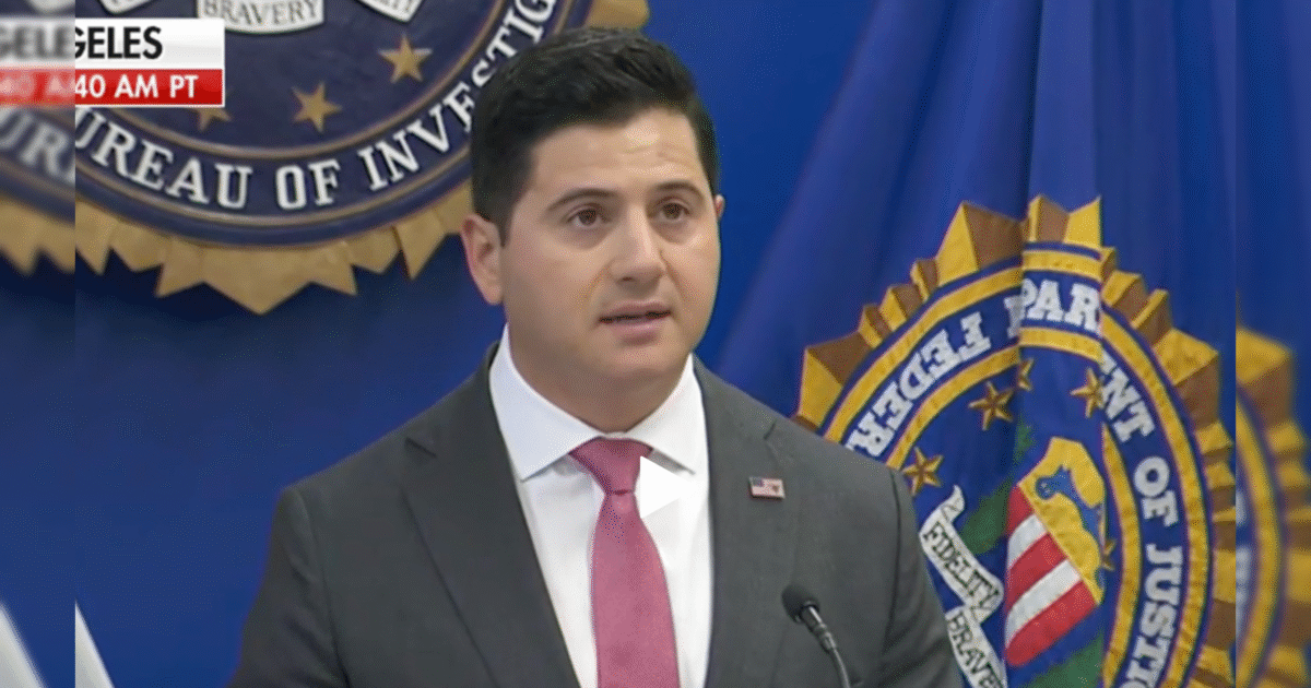 FBI official giving a press conference in front of the FBI seal and flags, discussing recent investigations and law enforcement efforts.