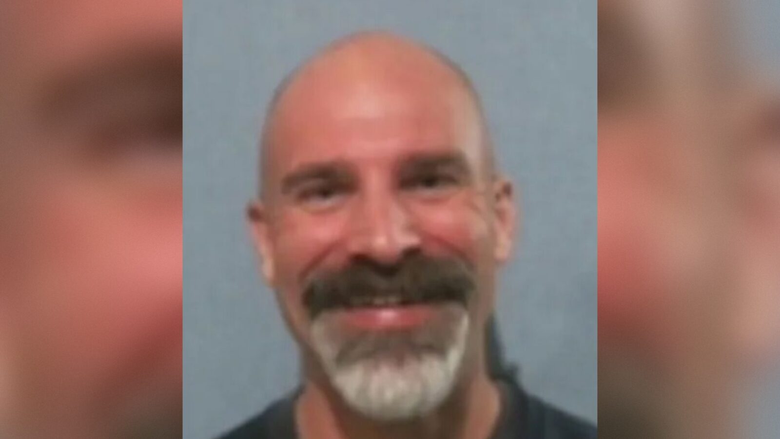 Smiling bald man with a goatee wearing a black shirt against a gray background.