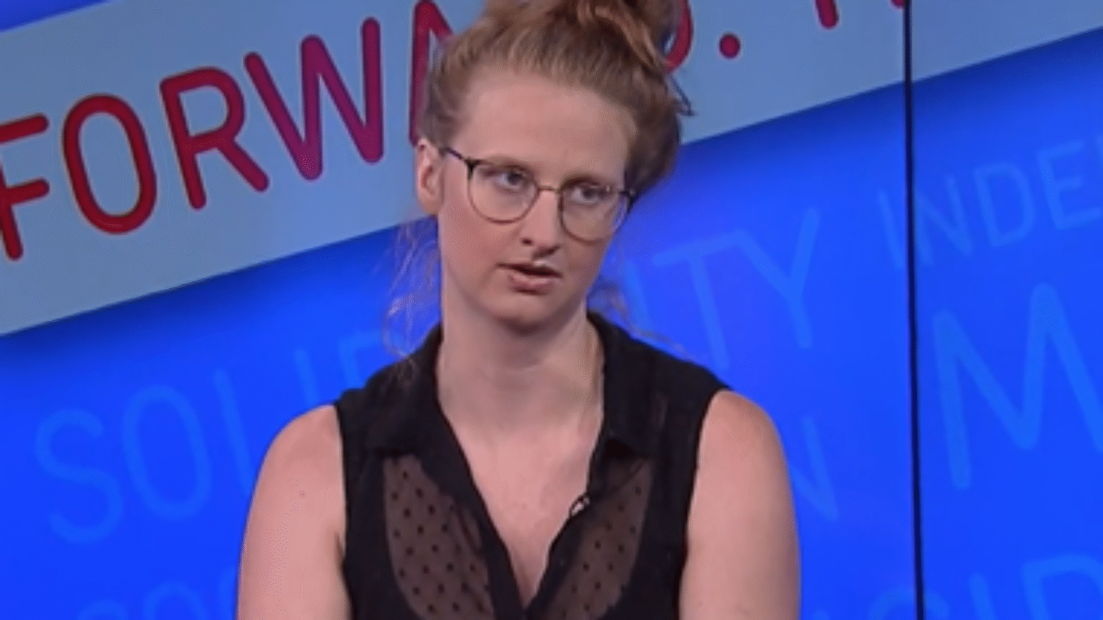 Person with glasses and a bun hairstyle sitting in front of a blue background with text promoting solidarity and community engagement.