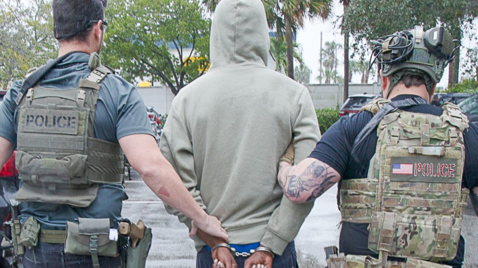 Police officers apprehending a suspect in handcuffs while wearing tactical gear in a public area.