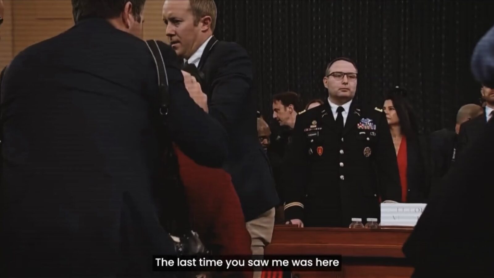 A tense moment during a congressional hearing with multiple figures in formal attire, highlighting the seriousness of the proceedings.