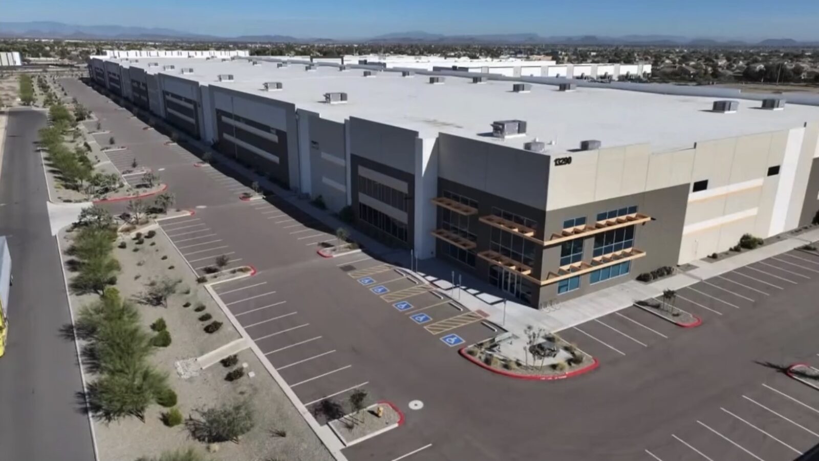 Aerial view of a large commercial warehouse with ample parking spaces and landscaped surroundings in a suburban area.