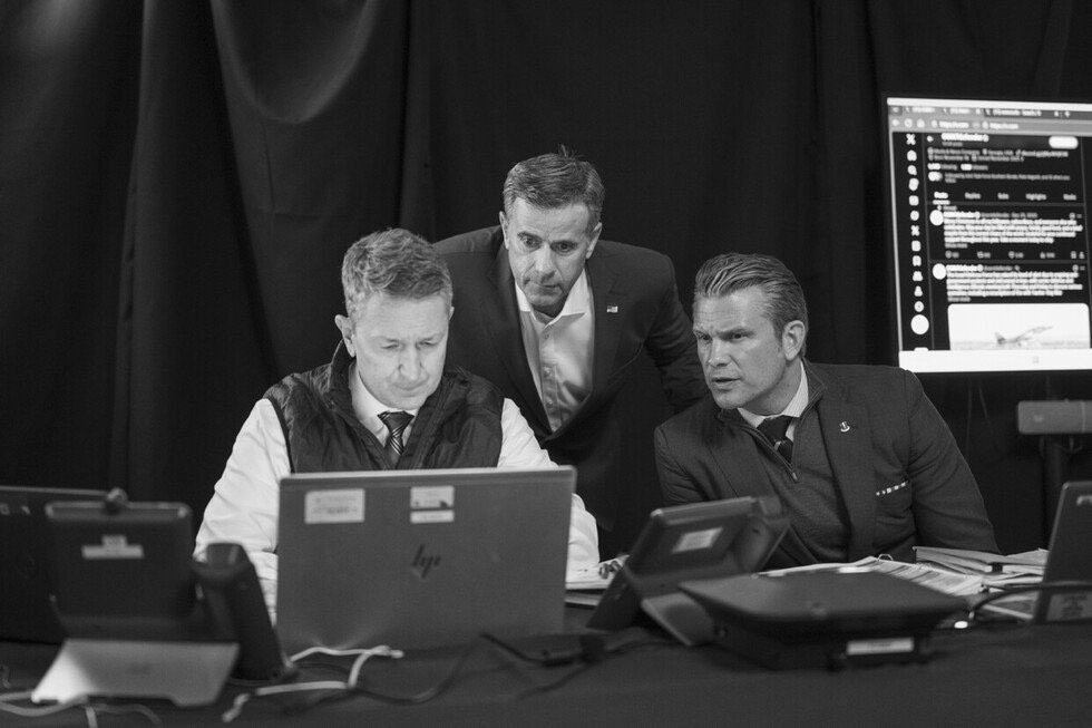 Three professionals engaged in a serious discussion while reviewing information on a laptop in a dimly lit room.
