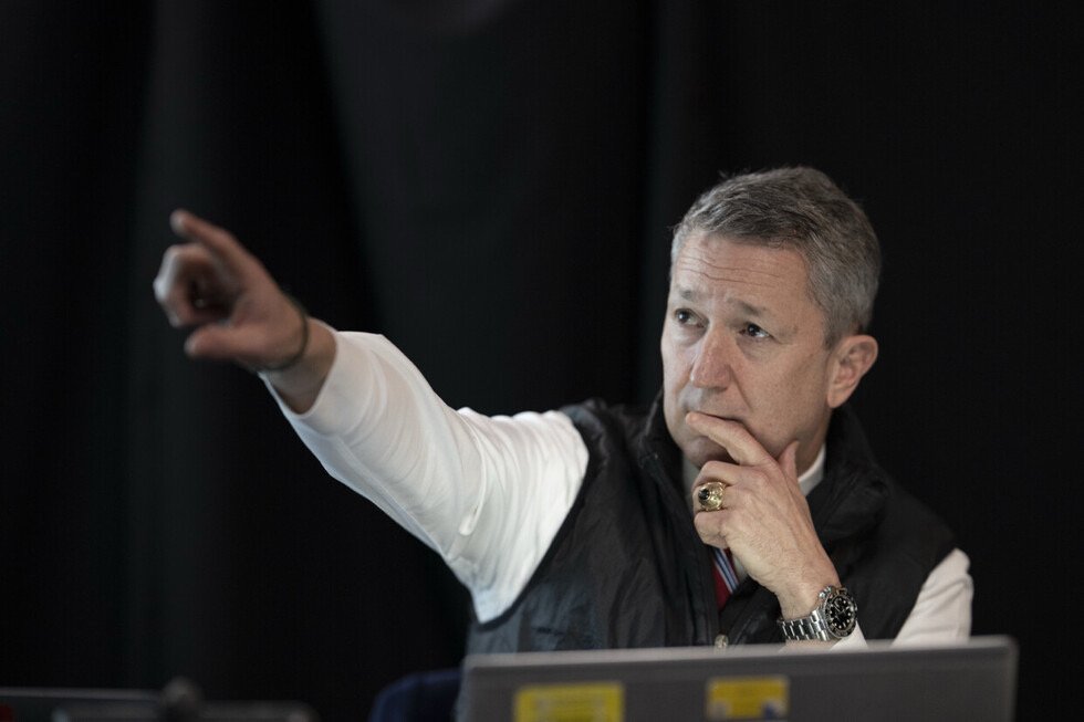 Business professional gesturing while deep in thought during a meeting or presentation, wearing a vest and displaying a ring.