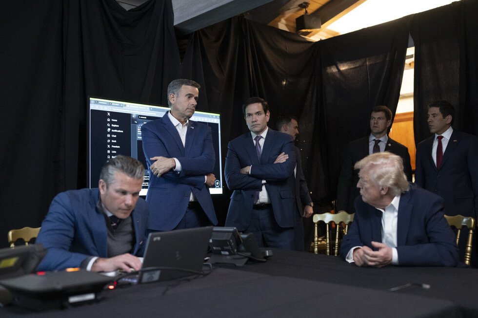 Group of political figures, including Donald Trump and Marco Rubio, gathered around a table with technology, discussing strategy in a dimly lit room.