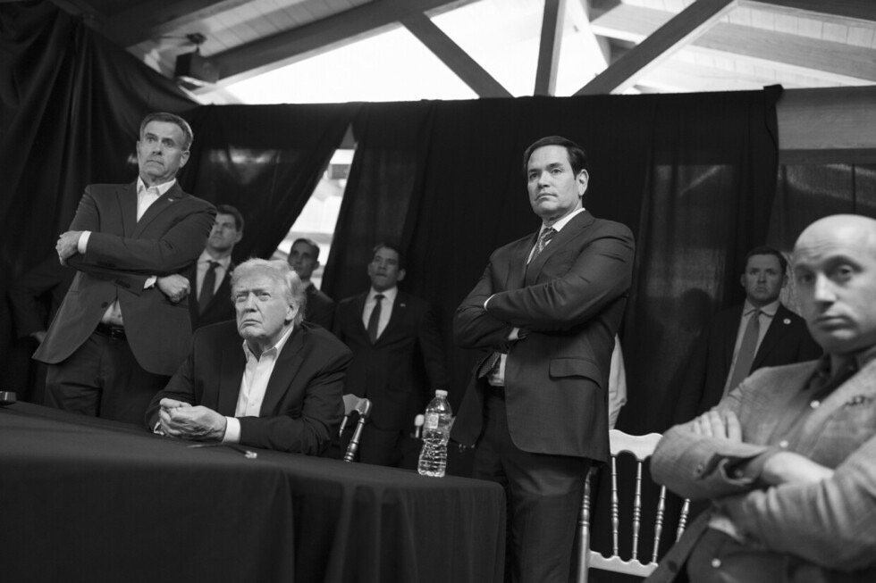 Donald Trump and several political figures observe a discussion at a table, conveying a serious atmosphere in a black and white setting.
