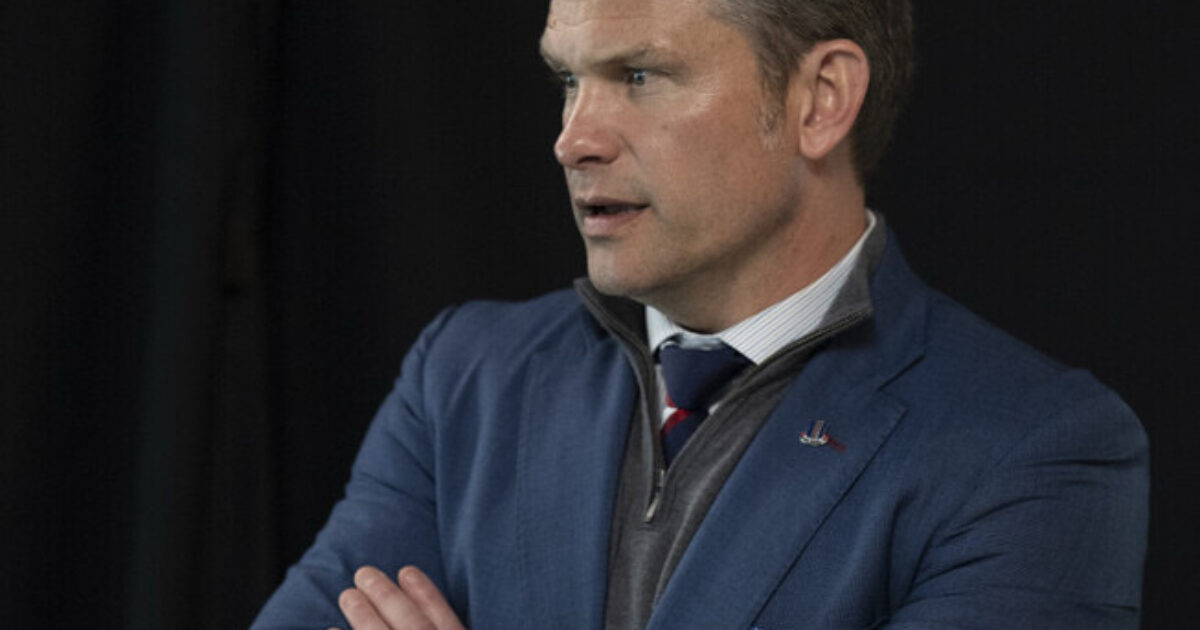 Man in a blue blazer with crossed arms, exhibiting a thoughtful expression against a dark backdrop.