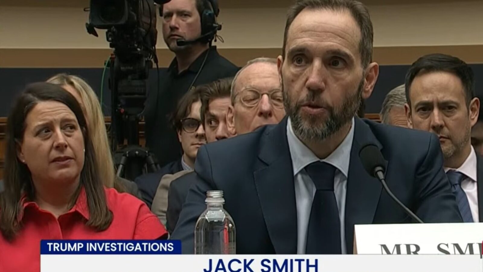 Jack Smith, former Independent Special Counsel, testifies during a congressional hearing on Trump investigations, with an audience and media present.