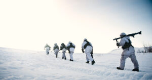 Soldiers in winter camouflage march through snow-covered terrain, demonstrating military training and readiness in a cold environment.