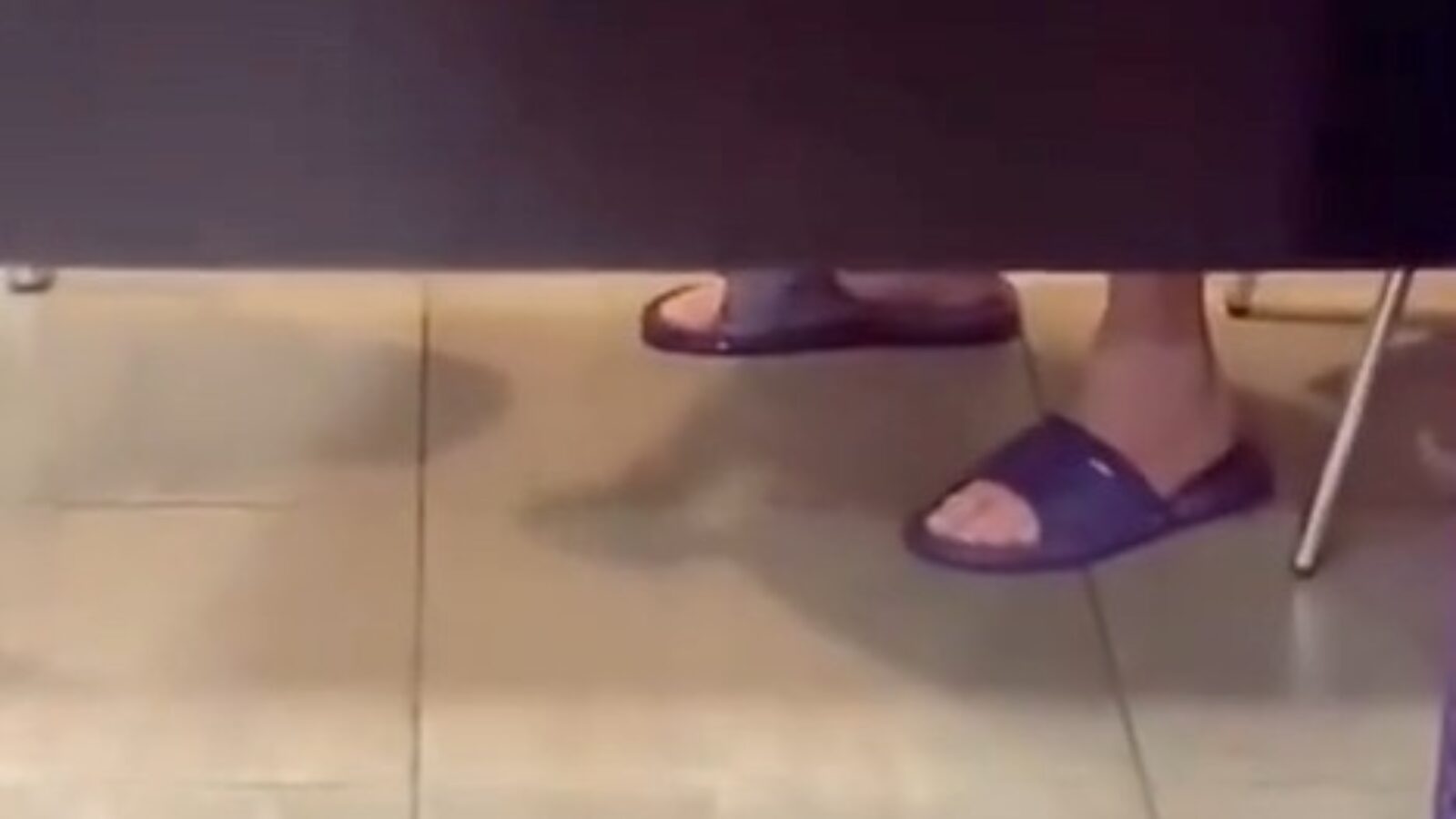 Person wearing purple slide sandals sitting at a table with tiled floor, partially visible from under the table.