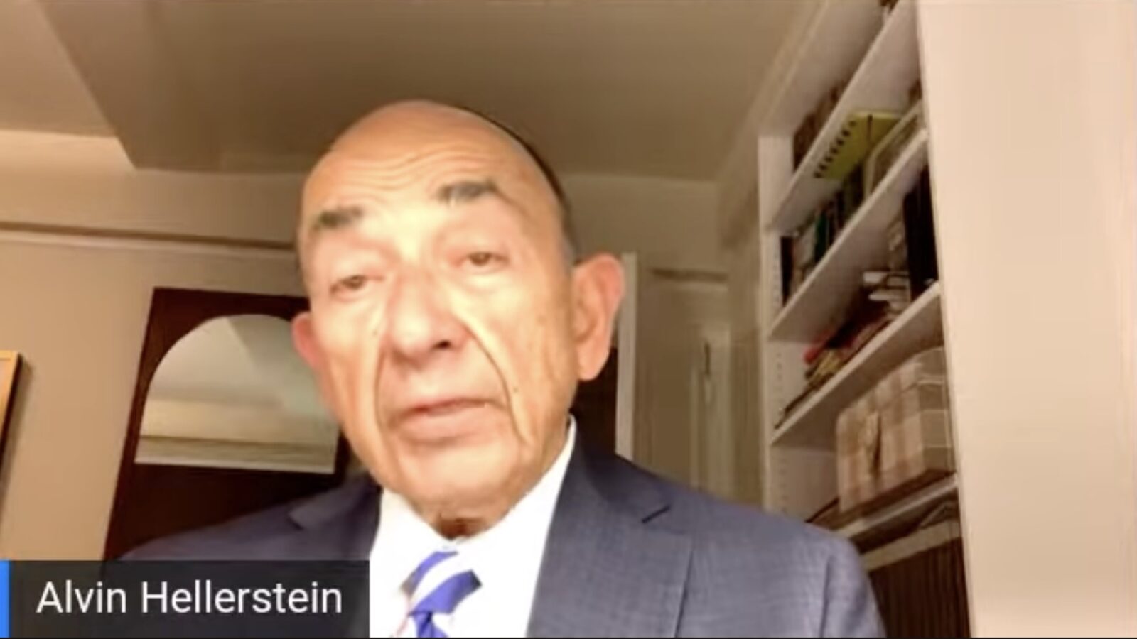Alvin Hellerstein speaking during a video conference, wearing a suit, with a bookshelf in the background.