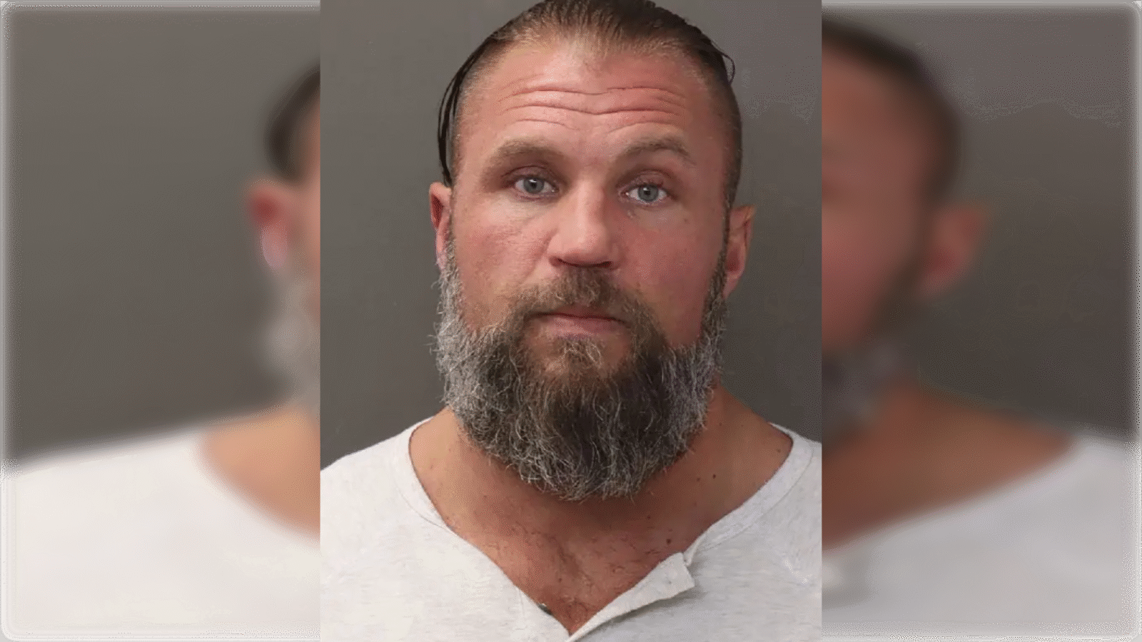 Mugshot of a man with a thick beard and short hair, wearing a gray shirt, against a neutral background.