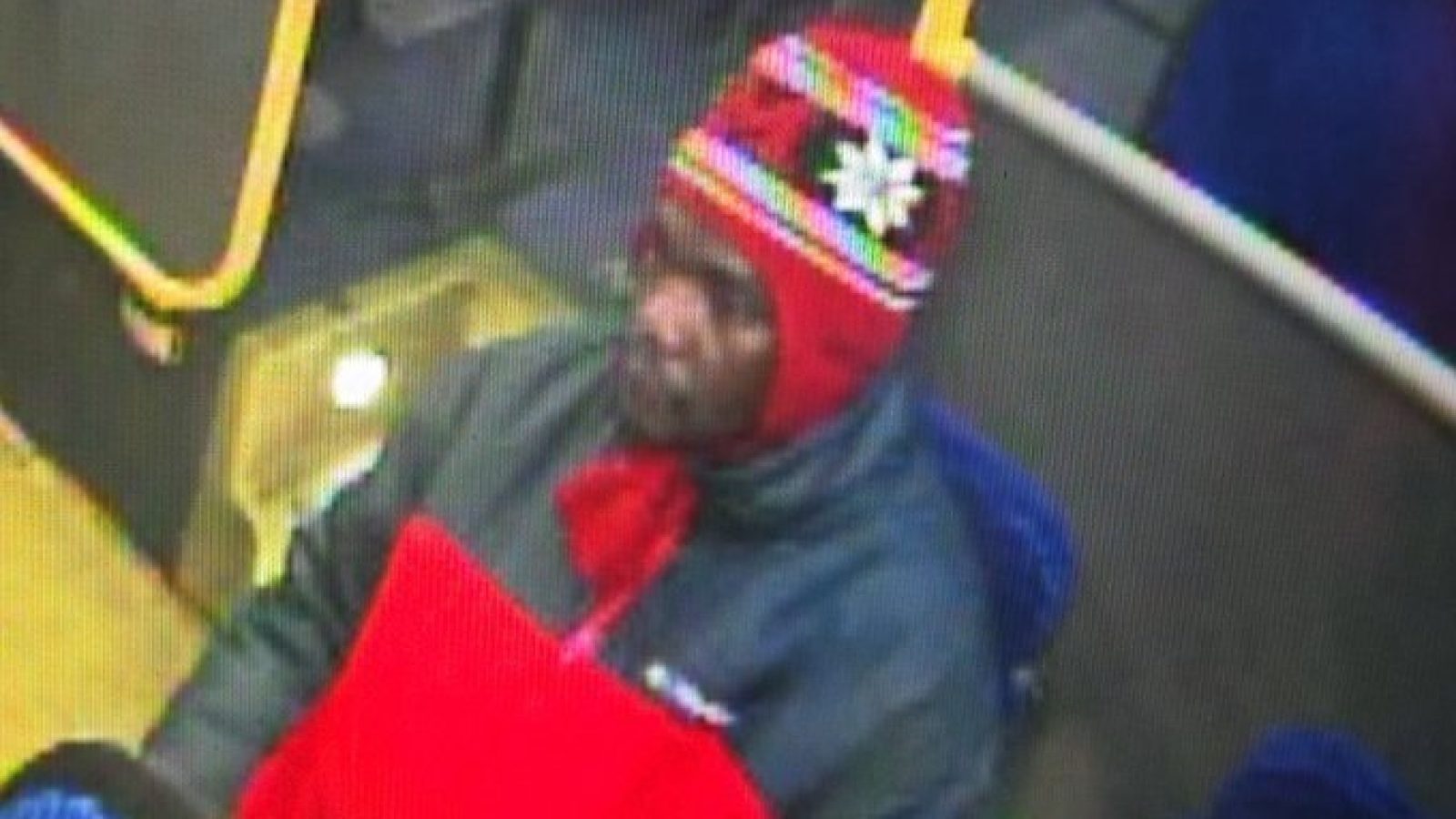 Man wearing a red and patterned beanie and a red jacket sitting on a bus.