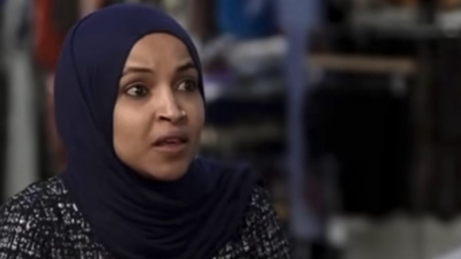 Woman in a hijab expressing concern during an interview, with a blurred retail background.
