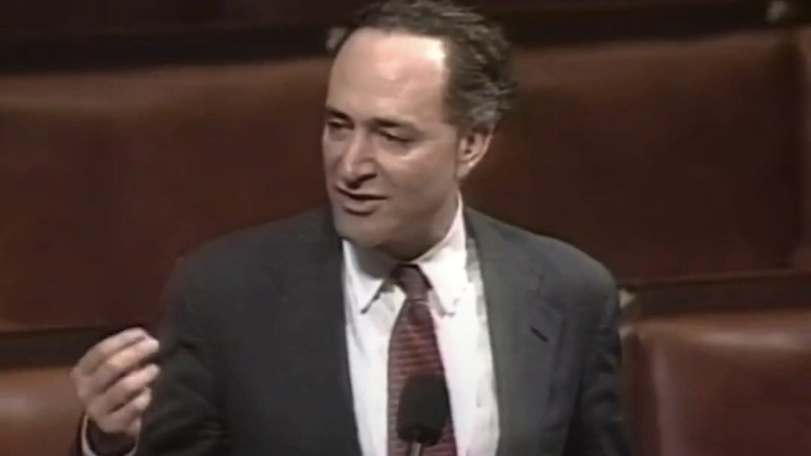 Politician speaking passionately at a podium in a legislative chamber, emphasizing key points during a debate.