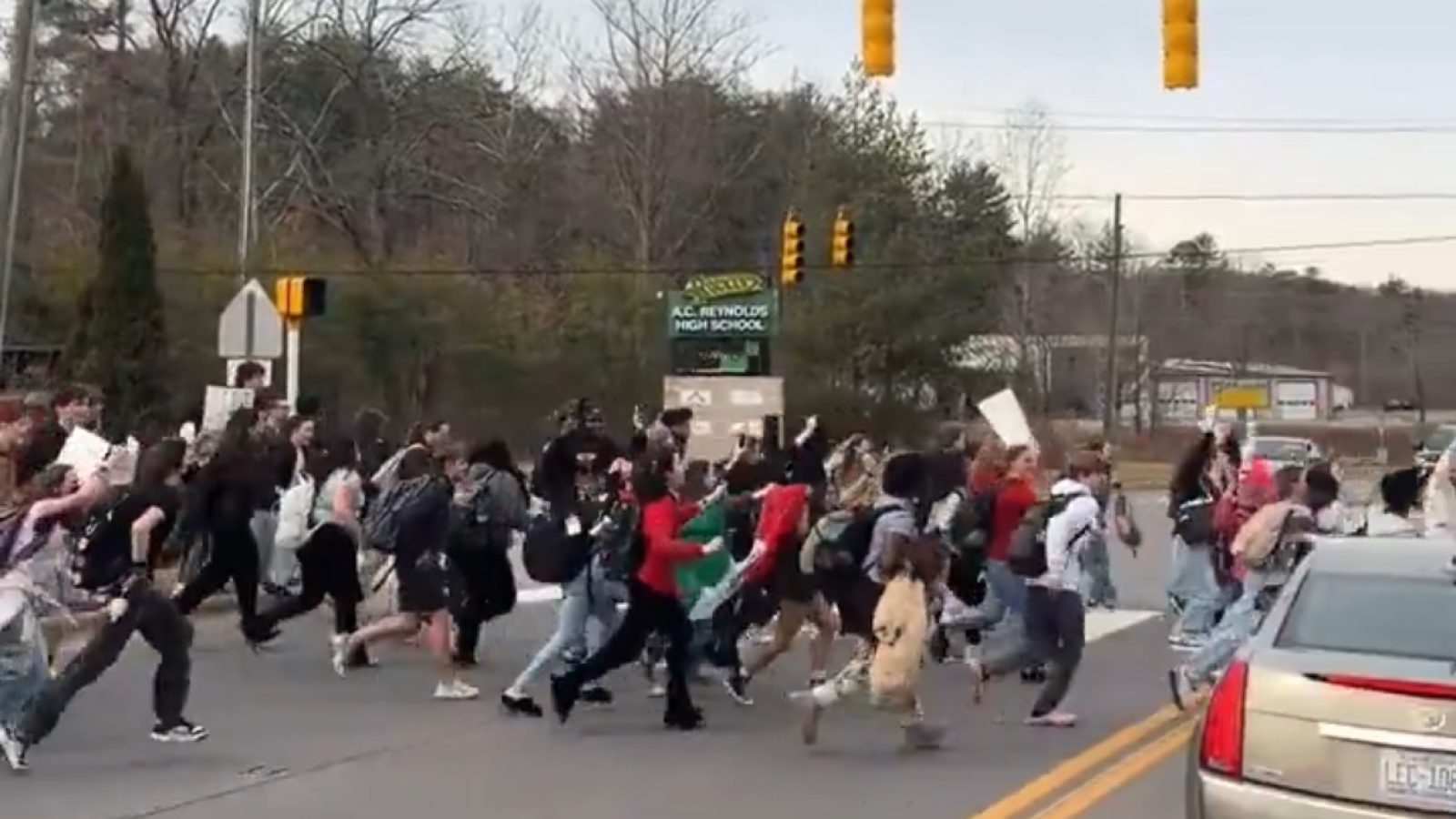 Students running across the street during a protest outside A.C. Reynolds High School, advocating for social change and awareness.