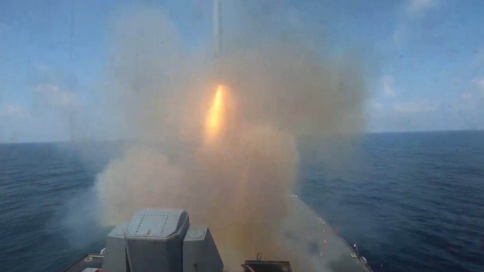 Missile launch from a naval ship, surrounded by smoke, over the ocean under a clear blue sky.
