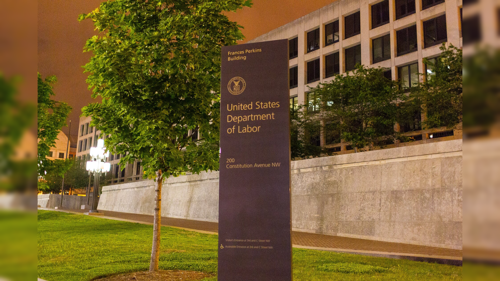 Signage for the United States Department of Labor located at 200 Constitution Avenue NW, illuminated at night with surrounding greenery.
