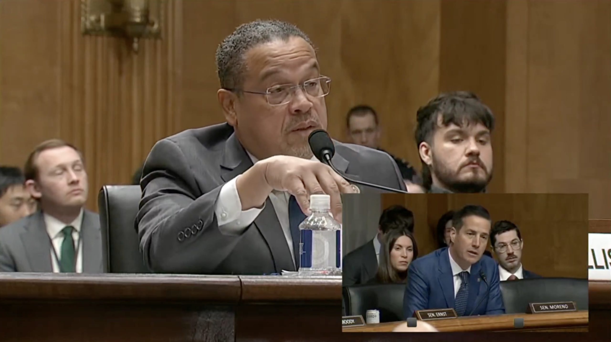 A congressional hearing with a speaker addressing the committee, while other attendees listen attentively in the background.