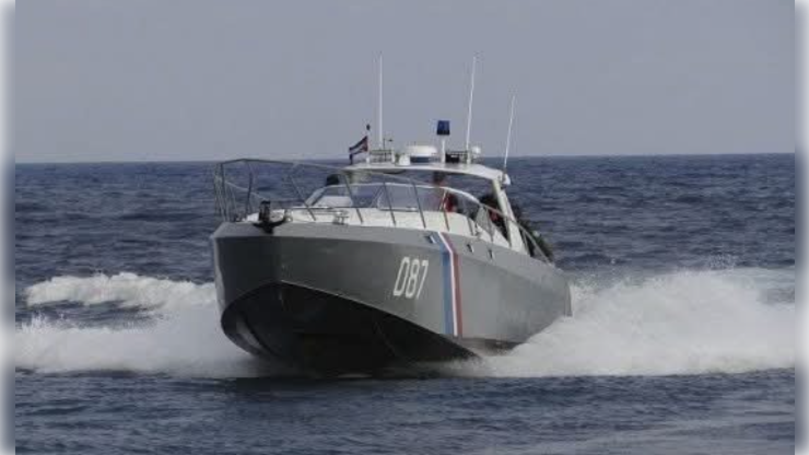 Gray patrol boat with the number 087 speeding across the ocean, creating waves and showcasing maritime security operations.
