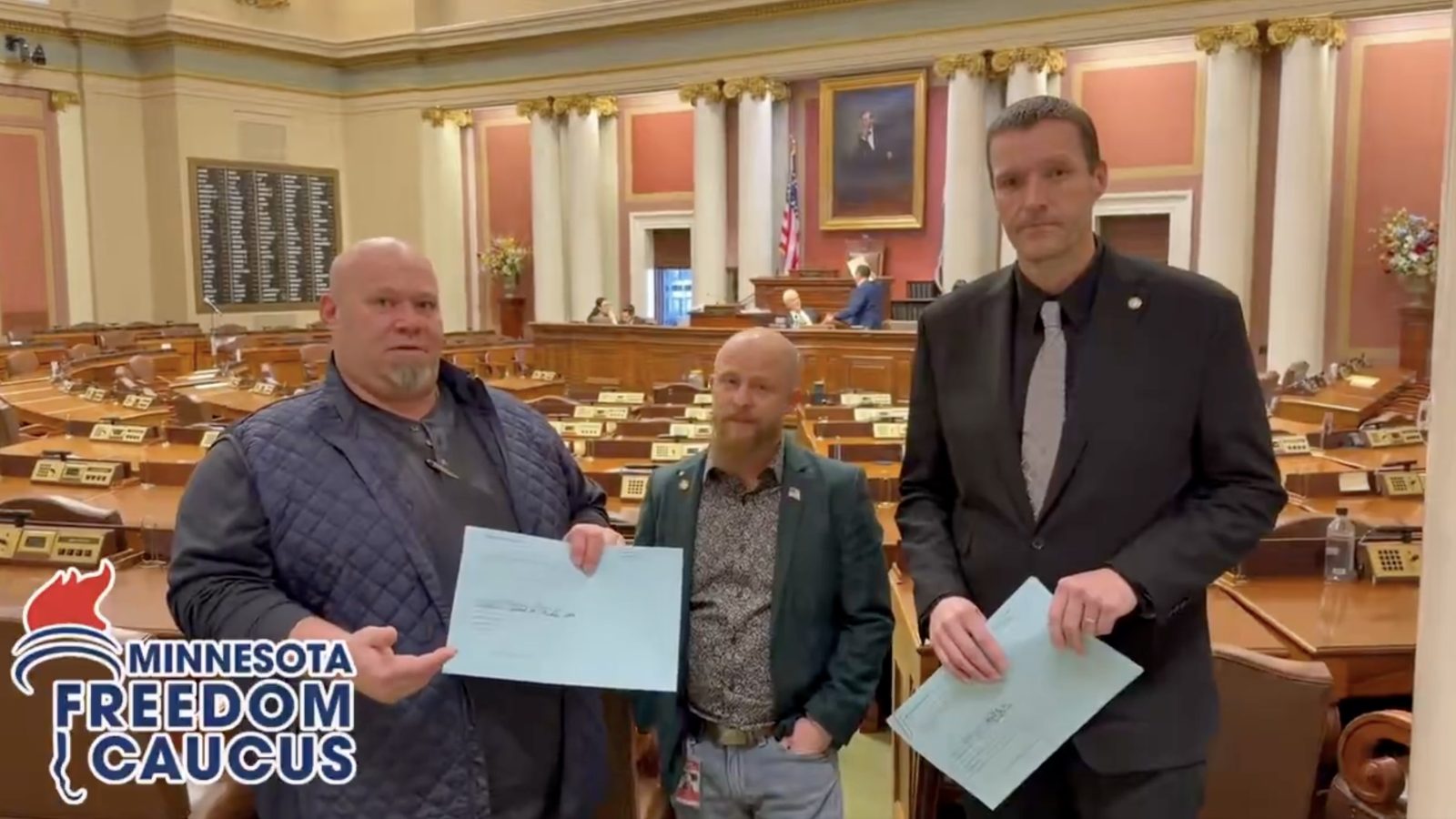 Three members of the Minnesota Freedom Caucus hold documents in a legislative chamber, emphasizing their involvement in state governance.