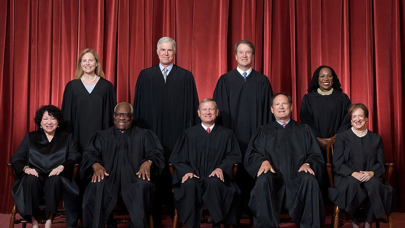 U.S. Supreme Court justices posing for an official group portrait, featuring nine members in black robes against a red curtain backdrop.