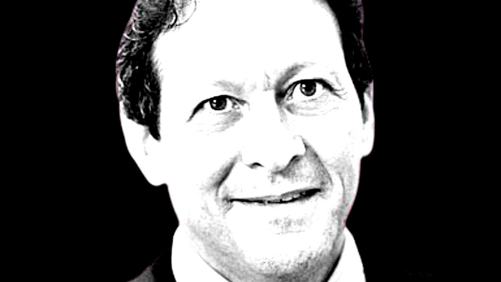 Black and white portrait of a smiling man with short hair, set against a dark background, conveying a professional demeanor.