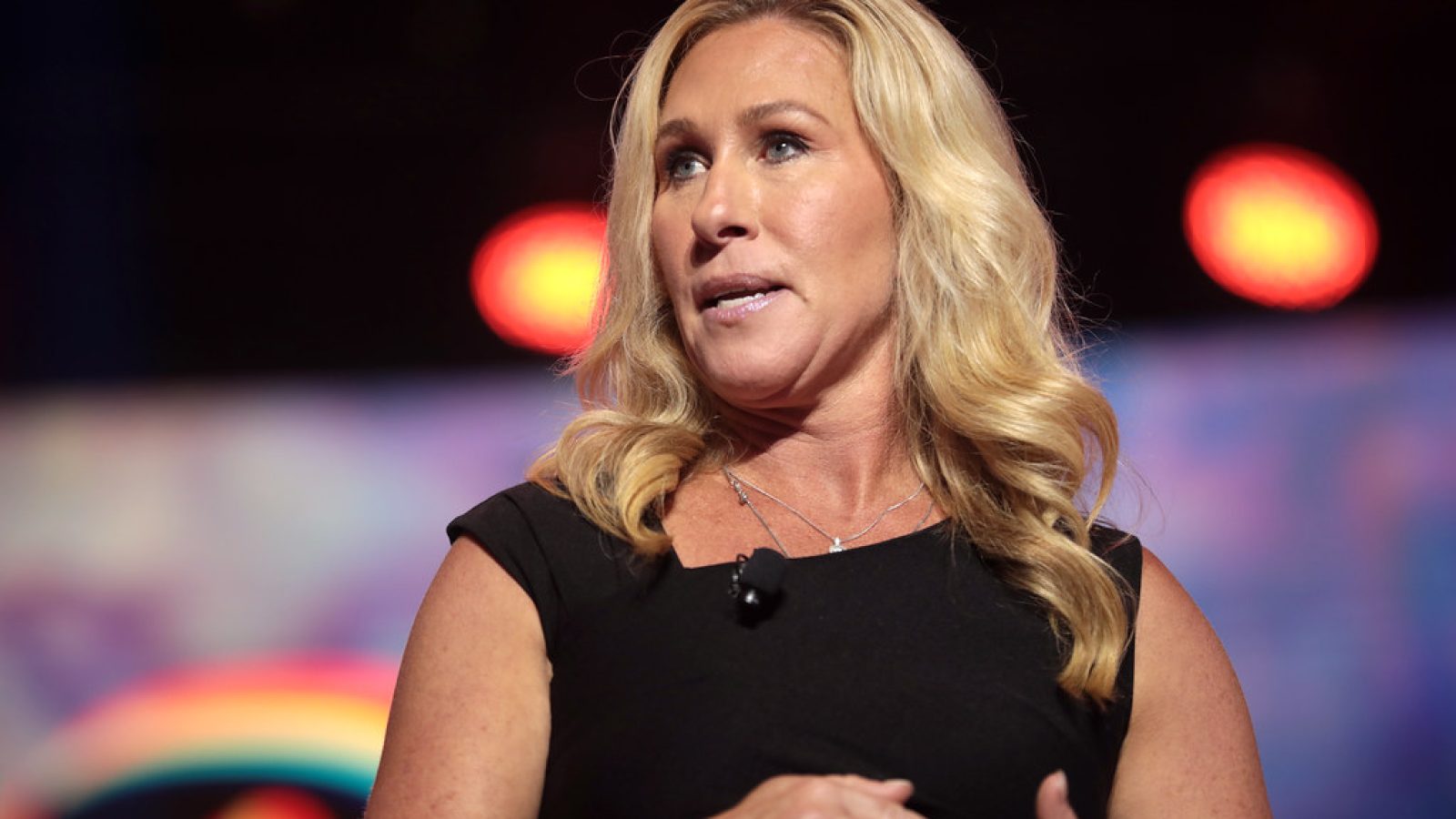A woman with long blonde hair speaks passionately at a conference, highlighting her role in political discussions.
