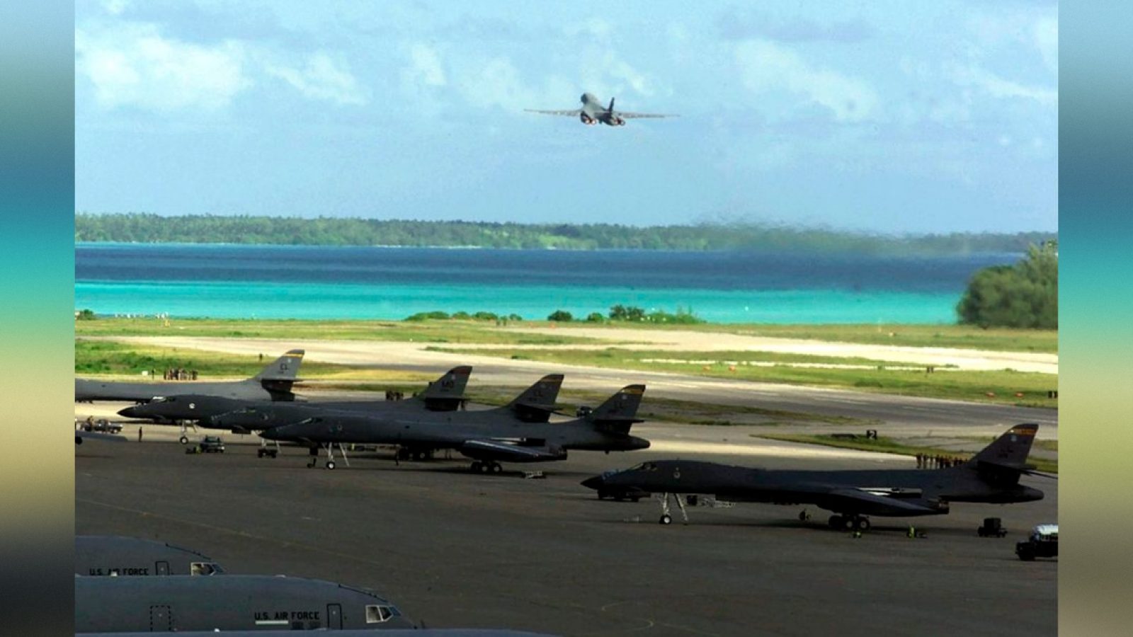 Military aircraft lined up on a runway with a tropical beach and ocean in the background, showcasing a blend of aviation and natural scenery.
