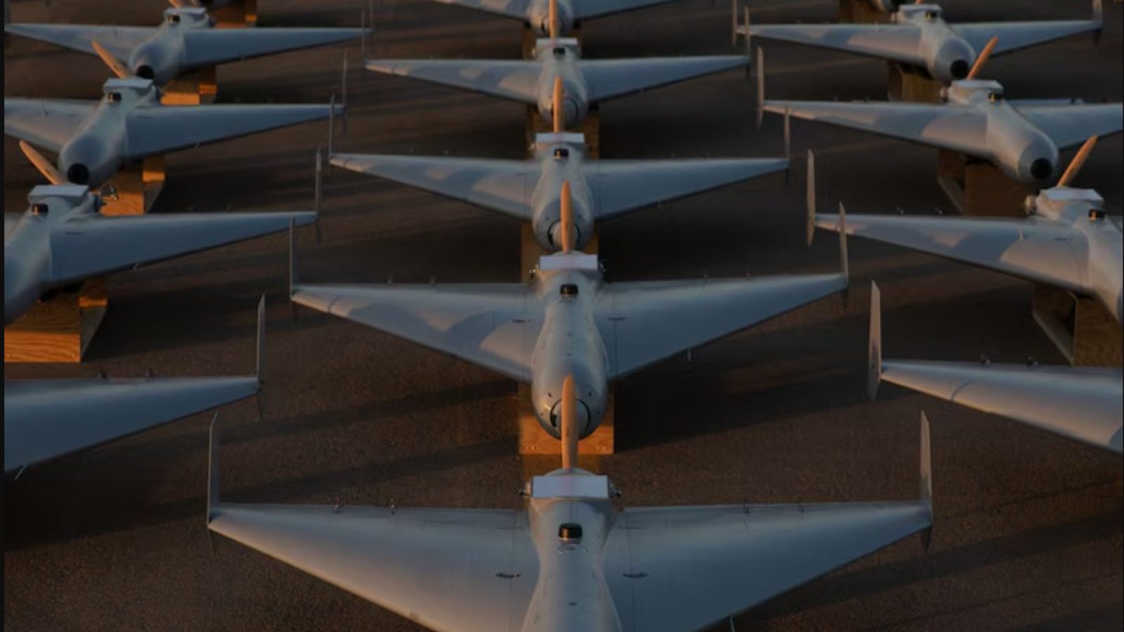 Rows of military drones parked on a runway, showcasing modern unmanned aerial vehicle technology in a military setting.