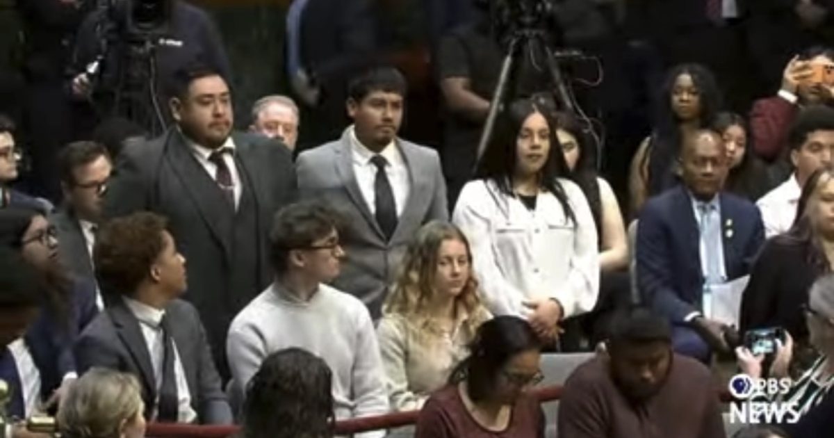 Diverse group of young adults and professionals attending a formal event, with cameras capturing the moment in a legislative setting.