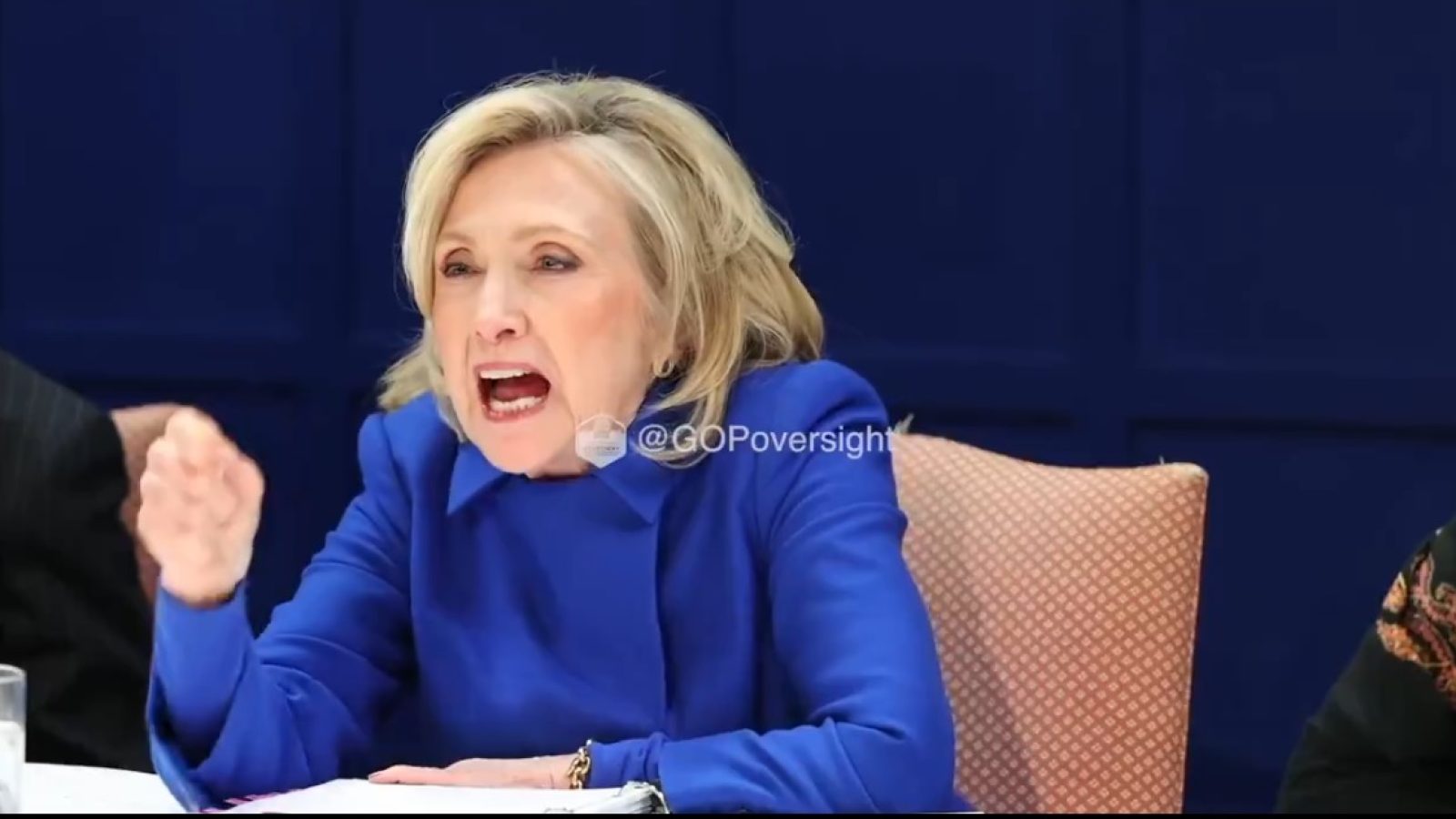 Hillary Clinton passionately speaks during a discussion, wearing a blue jacket, with a serious expression in a formal setting.