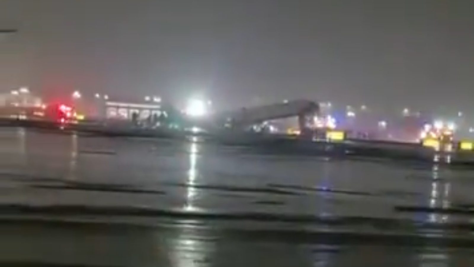 Emergency response vehicles on a wet airport runway during a nighttime incident with low visibility and scattered lights in the background.