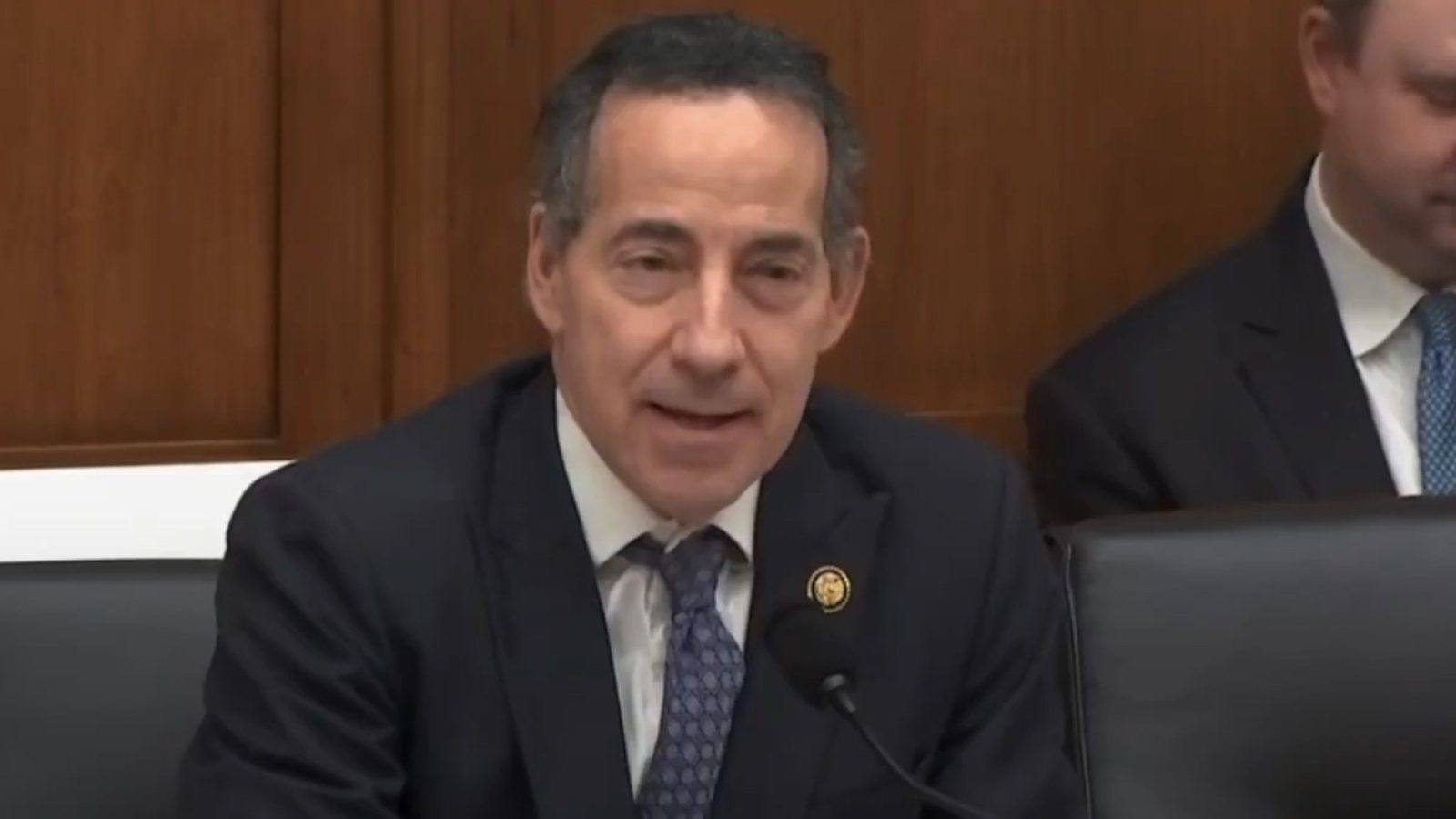Congressman Raskin speaking during a congressional hearing, seated at a table with water bottles and colleagues in the background.